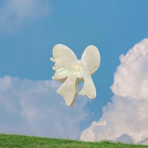 Pince à cheveux nœud papillon en acétate blanc iridescent sur fond de ciel bleu et d'herbe