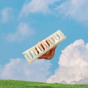 Close-up of wavy cream hair claw clip with pearlescent finish held against sky