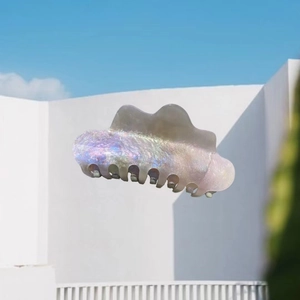 Cloud-shaped acetate hair claw clip with colorful pearlescent finish against a blue sky
