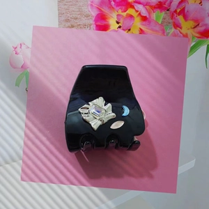 Pince à cheveux noire avec accents floraux argentés et cristaux sur fond rose