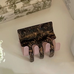 Detailed view of square acetate hair claw with marble texture and pink inner teeth