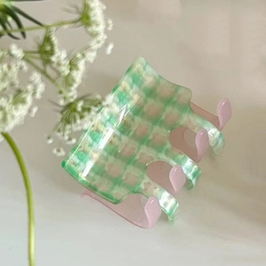 Detail of green and white checkerboard hair claw clip with transparent pink teeth texture