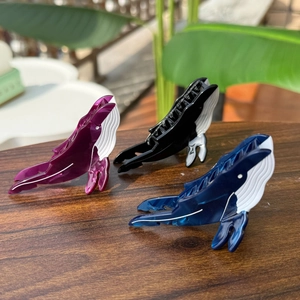 Détail de trois pinces à cheveux en acétate en forme de baleine, violette, noire et bleue