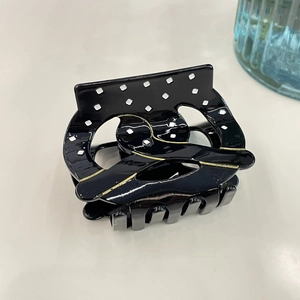 Close-up of black acetate hair claw clip with white polka dots and gold line details