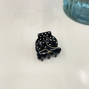Detail of small black acetate hair claw with white polka dots and gold wavy line patterns