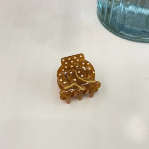 Detail of amber acetate hair claw with white polka dots and gold line accent