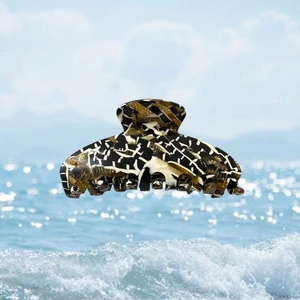 Détail d'une grande pince à cheveux en acétate avec motif abstrait effet glace devant l'océan