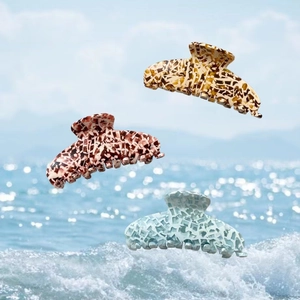 Trois grandes pinces à cheveux en acétate marbré présentées sur un fond de plage estivale