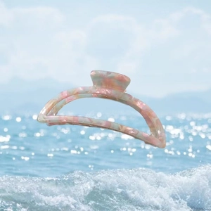 Close-up of marble acetate hair claw clip floating over a sparkling ocean background