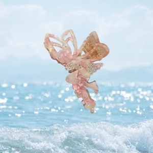 Pink marbled acetate butterfly hair claw clip with rhinestones shown by the ocean