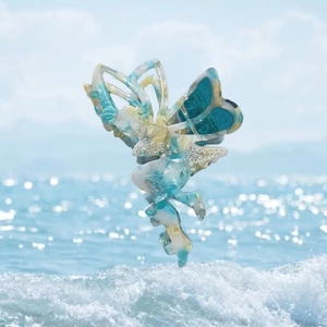 Blue and white butterfly hair claw clip with rhinestones shown against a beach background
