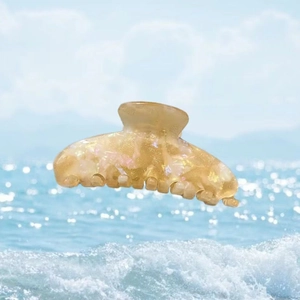Pince à cheveux scintillante en acétate doré champagne sur fond de plage estivale