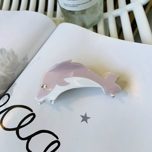 Pince à cheveux dauphin en acétate rose avec détail d'étoile sur fond lifestyle chic