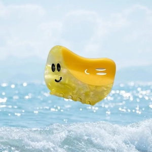 Pince à cheveux jaune en acétate avec visage souriant et texture marbrée sur fond marin