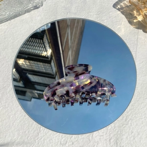 Elegant purple marbled acetate hair claw clip reflecting a clear blue sky on a mirror