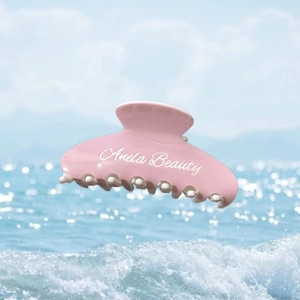 Pince à cheveux rose en acétate avec texte Anela Beauty blanc sur fond d'océan bleu