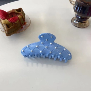 Détail d'une pince à cheveux bleu clair à motif losanges et perles sur une table