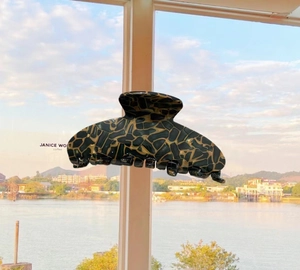 Large acetate hair claw clip with amber mosaic pattern against a sunny river background
