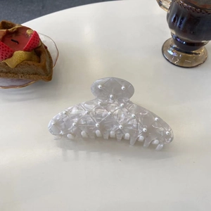 Vue détaillée d'une pince à cheveux en acétate marbré avec perles sur table blanche