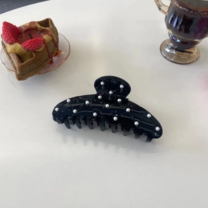 Gros plan d'une pince à cheveux noire matelassée avec des perles blanches élégantes