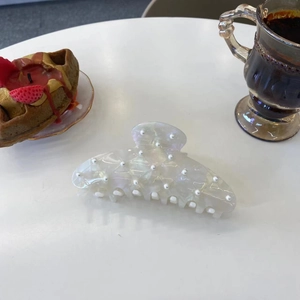 Pince à cheveux élégante avec perles et reflet nacré posée sur une table de thé chic