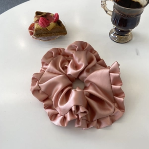 Chouchou élégant en satin or rose surdimensionné avec bords volantés sur bureau blanc