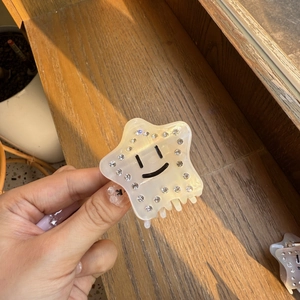Pinza per capelli a stella in acetato con faccina e strass su sfondo di legno naturale