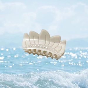 Pince à cheveux lotus minimaliste crème avec perles sur fond de plage d'été et océan