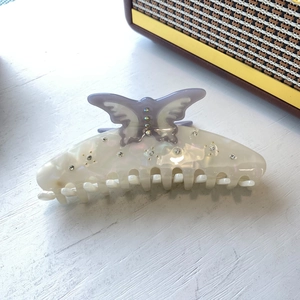 Large cream acetate hair claw clip with purple butterfly rhinestone ornament on wood desk