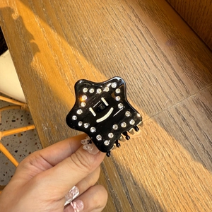 Dettaglio molletta a stella in acetato nero con strass e simpatico viso sorridente