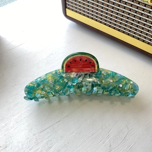 Macro detail of watermelon claw clip with green marble texture and small white rhinestones