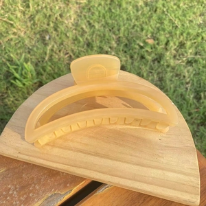 Detail of large amber resin crescent hair claw clip on a minimalist wooden stand