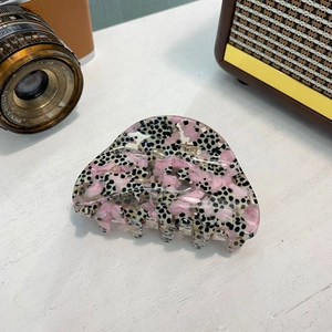 Gros plan sur la pince à cheveux en acétate rose et noir dans un décor rétro raffiné