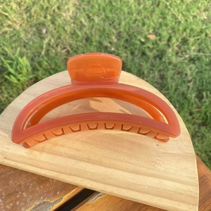 Minimalist glossy orange crescent hair claw clip for women displayed on wood base
