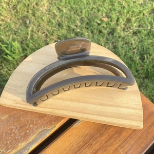 Macro detail of a large grey crescent hair claw clip on wooden stand with garden background