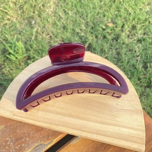 Close-up of a large dark red crescent hair claw clip on a wooden display stand