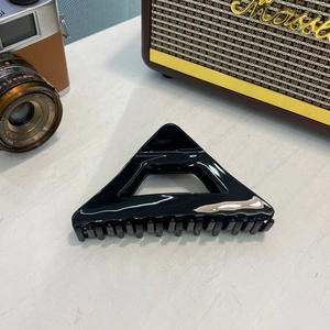 Elegant glossy black acetate triangular hair claw clip with cutout in retro lifestyle setting