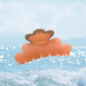 Close-up of pink and grey acetate hair claw clip with cloud wave design on beach background