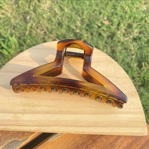 Detailed view of amber tortoiseshell hair claw clip with metal spring on wooden base