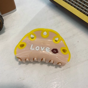 Pince à cheveux en acétate rose et jaune avec lettrage Love sur table en bois