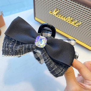 Detail of tweed bow hair claw with pearl trim and large crystal center on black ribbon