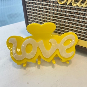Vue détaillée de la pince à cheveux cœur en acétate jaune avec lettrage love en 3D