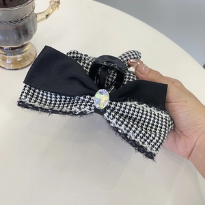 Macro view of the bow claw clip with houndstooth tweed, satin ribbon, and a crystal rhinestone