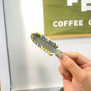 Close-up of a handmade knit hair clip with grey, yellow, and white wool yarn textures