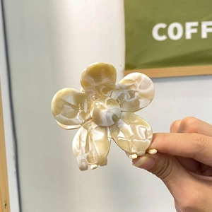 Détails de la texture marbrée crème sur la pince à cheveux en forme de fleur en acétate