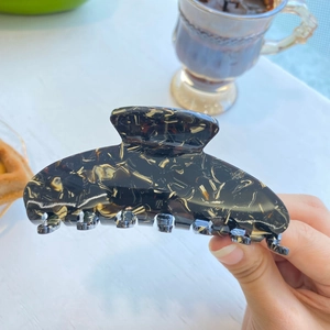 Large acetate hair claw clip with black and beige marble pattern in a lifestyle setting