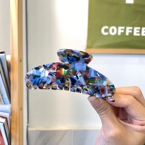 Grande pince à cheveux en acétate coloré avec texture marbrée tenue à la main en décor