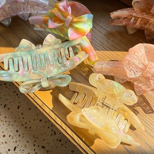 Iridescent acetate hair claw clips with bow design reflecting natural sunlight