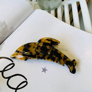 Détail de la pince à cheveux dauphin en écaille de tortue posée sur un magazine blanc