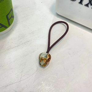 Détail d'un chouchou marron avec breloque cœur en résine, feuille d'or et texture ambrée